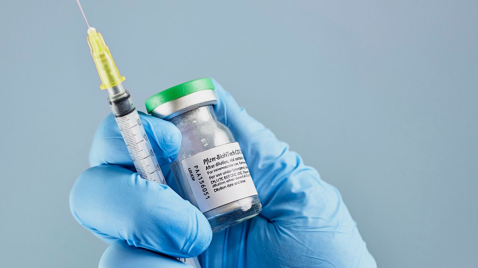 Mão com luva azul segura uma seringa e um frasco da vacina Pfizer-BioNTech contra a Covid-19